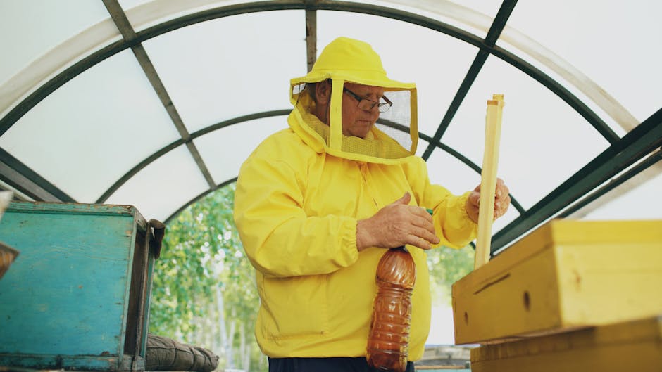 Beekeeper in protective yellow suit handling honey equipment indoors.
