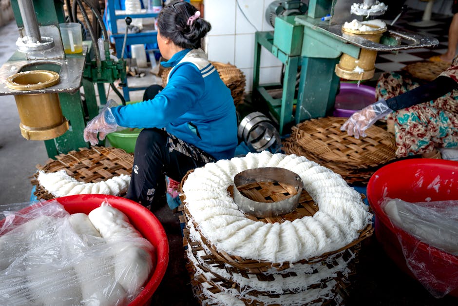 Anonymous workers making noodle on metal machines near wooden covers on manufacture in Vietnam