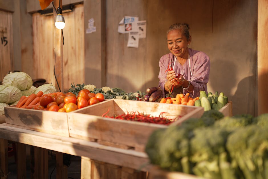 A senior woman selling fresh produce at an outdoor market stand in warm light.